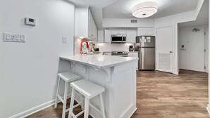 A modern kitchen with white cabinetry, a central island with bar stools, and built-in appliances.