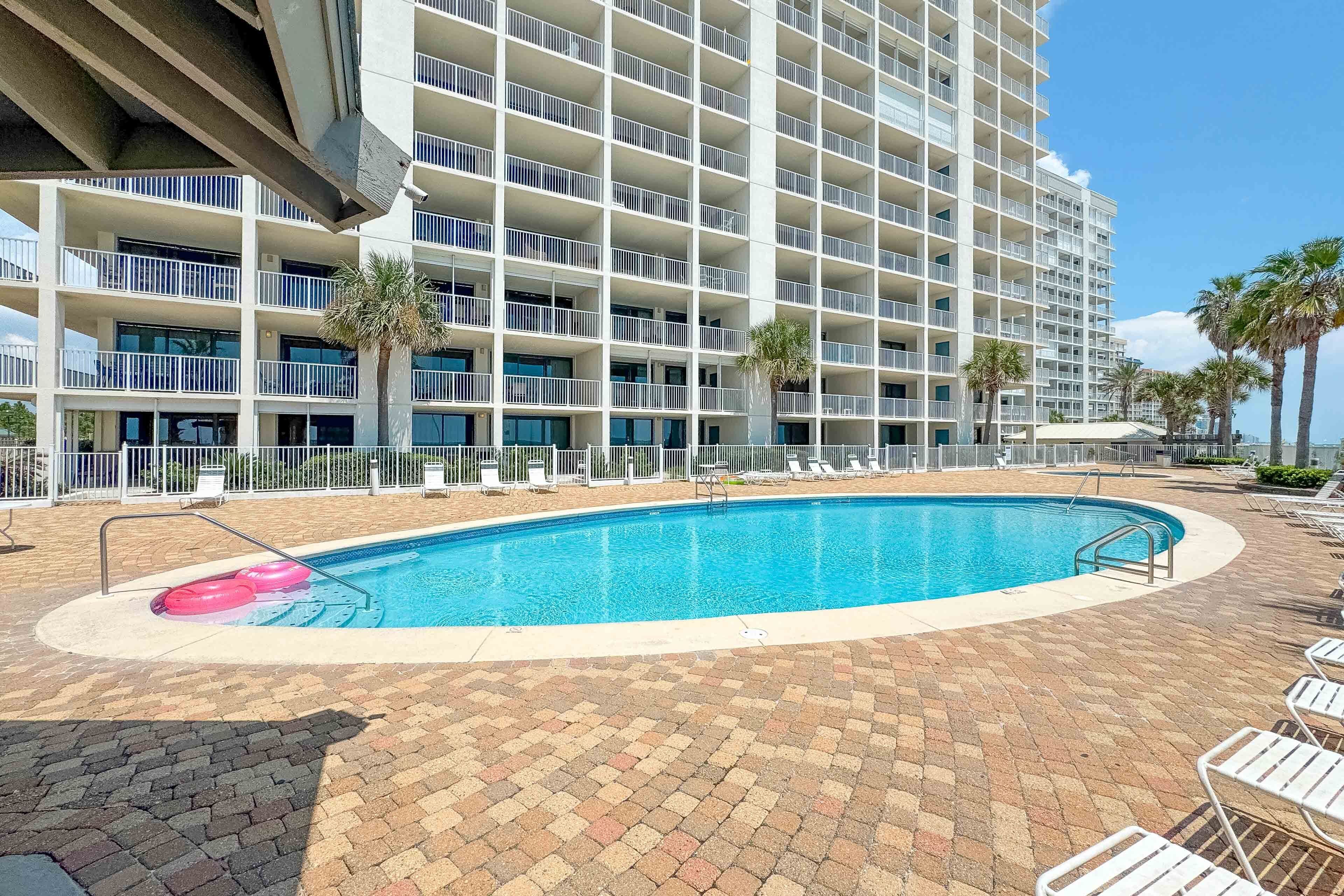 A hotel with a large pool, multiple balconies, and palm trees.