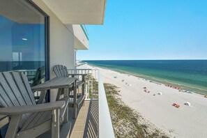 Un balcone con due sedie che si affaccia su una spiaggia con ombrelloni e vista libera sull'oceano.
