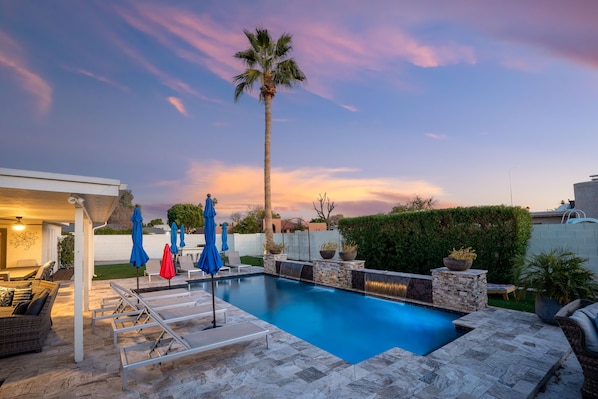 A swimming pool with lounge chairs and umbrellas, surrounded by stone walls and potted plants.