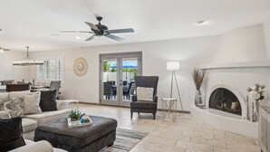 A spacious living room with a fireplace, a ceiling fan, and a dining area visible through glass doors. - The Bridle is Right | Saltwater Pool | Backyard Games (Mesa)
