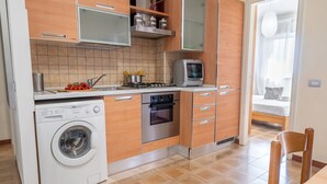 A compact kitchen with a washing machine, stove, oven, and a small television. - Casa Vacanza La Rosa (Giardini Naxos)