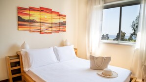 A neatly made bed with white linens, a bedside table with a lamp, and a view of the sea through a window. - Casa Vacanza La Rosa (Giardini Naxos)