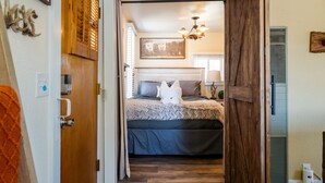 Une chambre à coucher avec un lit, une porte en bois, un mur blanc, un luminaire au plafond et une fenêtre.