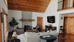 Un ampio soggiorno con soffitto in legno a vista, un camino in pietra, un televisore montato a parete e una zona relax con divano e tavolino.