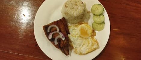 Un plato con arroz, un huevo frito, un trozo de carne y rodajas de pepino.