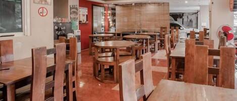 Un interior de restaurante con mesas y sillas de madera, piso de baldosas y un ventanal grande.