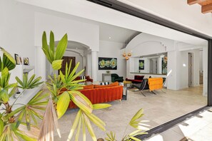 A spacious living area with a modern sofa, a dining table, and a large mirror. There are potted plants and a fireplace.