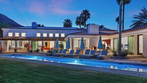 A resort with a swimming pool, lounge chairs, and palm trees.