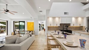 A modern kitchen with white cabinets, a central island, and a dining area with a sofa and chairs.
