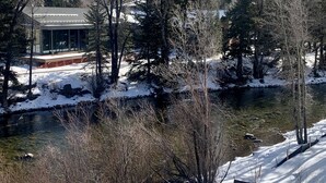 A modern building with large windows, surrounded by snow-covered trees and a river. - New! Luxury Riverfront Retreat with Mountain Views (Silverthorne)