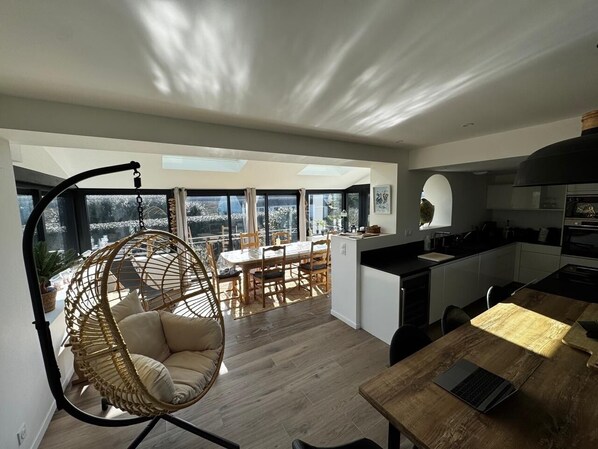 A modern kitchen with a dining area, a hanging chair, and a view of the outdoors.