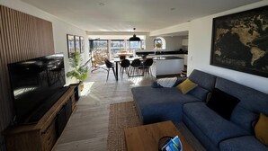 A modern living room with a large flat-screen TV, a sofa, and a dining area with chairs and a table. - "villa Bonheur", Maison Contemporaine, Idéale en Famille, à 300m de la Plage (Lampaul-Plouarzel)