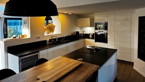 A modern kitchen with a central island, black pendant lighting, and white cabinetry. - "villa Bonheur", Maison Contemporaine, Idéale en Famille, à 300m de la Plage (Lampaul-Plouarzel)
