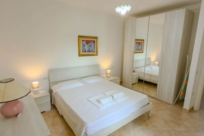 A hotel room with a bed, bedside lamps, a mirror, and a painting on the wall.