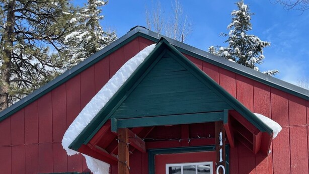 A red wooden building with a green roof and a white door, surrounded by snow.