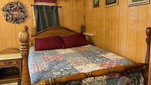 A wooden-paneled bedroom with a bed, a nightstand, a dresser, and a decorative wreath.