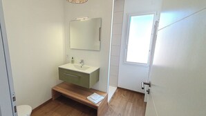 Ein kleines, kompaktes Badezimmer mit einem weißen Waschbecken, einem Spiegel und einer hölzernen Sitzbank.