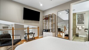 A modern bedroom with a large bed, a TV mounted on the wall, and a walk-in closet with a mirror. - The Fairchild Haus | 30 Acres, Sauna, EV Charger (Logan)