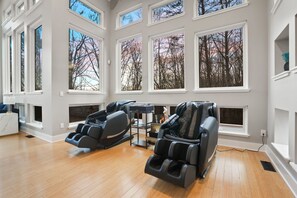 A room with two massage chairs, large windows, and a view of trees.