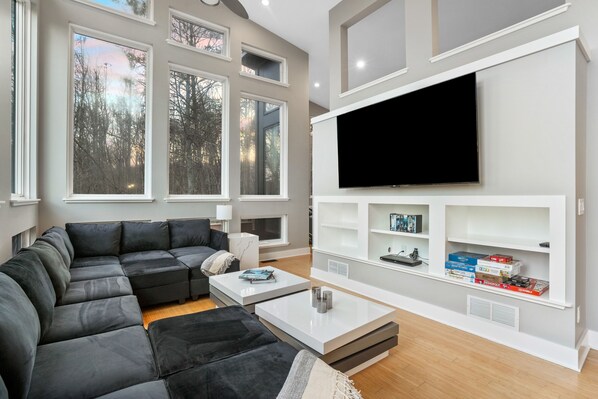 A modern living room with a sectional sofa, a coffee table, and a flat-screen TV mounted on the wall.