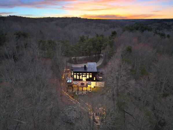 A cabin with a deck and outdoor seating area, surrounded by forest.