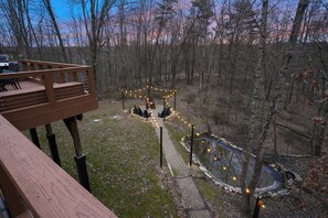 A deck with outdoor seating and a fire pit area surrounded by trees.