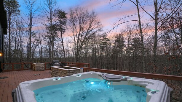 A hot tub on a wooden deck with a view of trees and a sunset. - The Fairchild Haus | 30 Acres, Sauna, EV Charger (Logan)