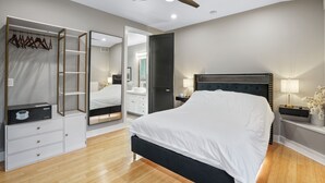 Ein Schlafzimmer mit Bett, Kleiderschrank, Spiegel, Deckenventilator und Nachttisch mit Lampe.