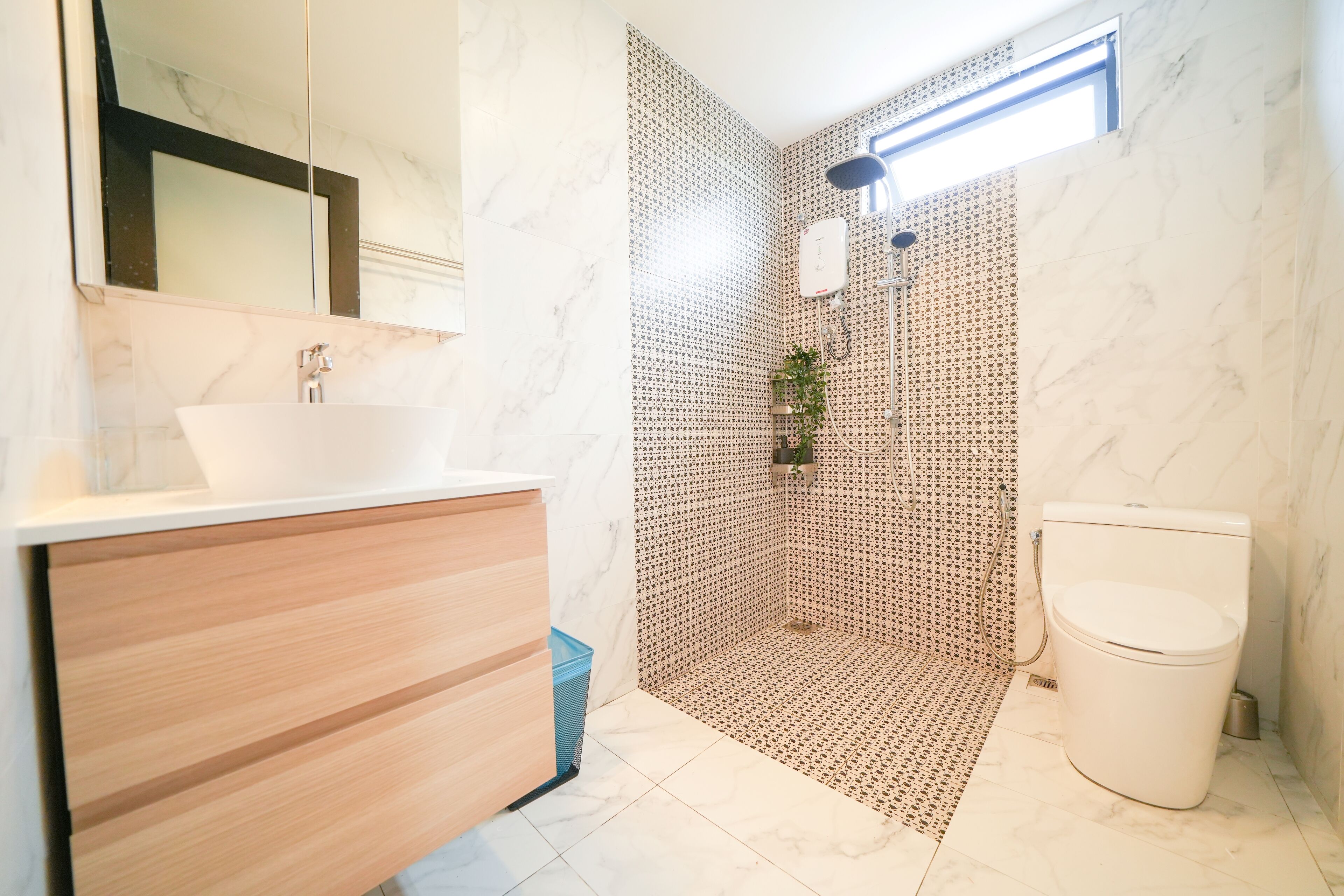 A modern bathroom with a wooden vanity, a white sink, a shower with a patterned wall, and a toilet.