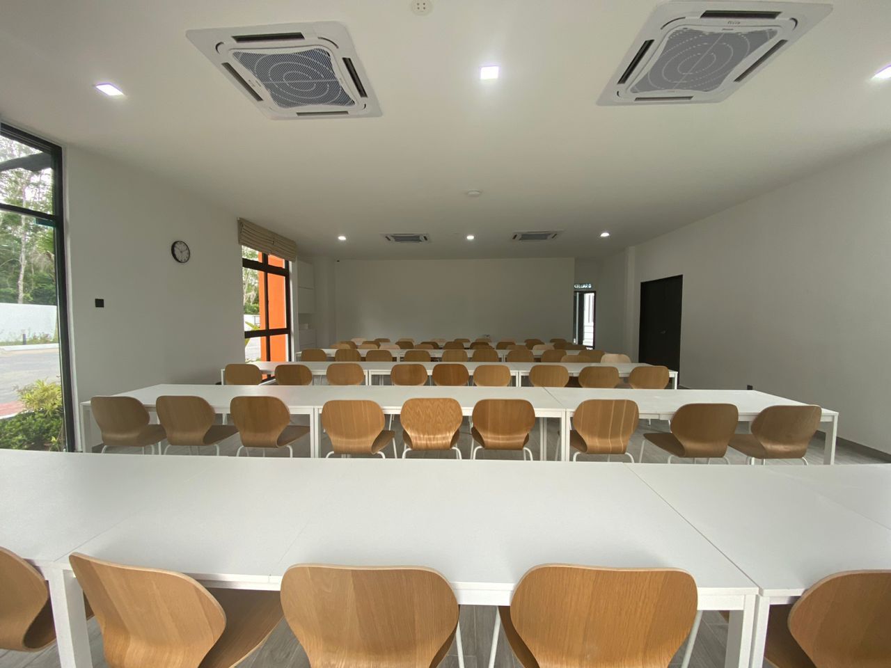 A conference room with white tables and brown chairs, large windows, and ceiling vents.