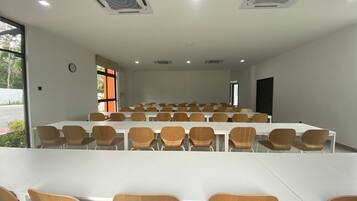 A conference room with white tables and brown chairs, large windows, and ceiling vents.