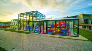 Une structure moderne en verre abritant une aire de jeux à l’intérieur, le tout se détachant sur un ciel dégagé.