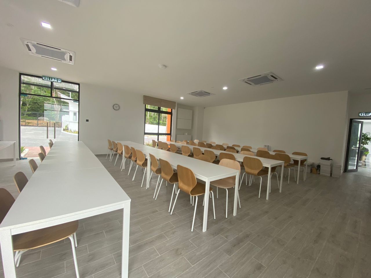 A conference room with long tables and chairs, large windows, and a view of the outdoors.