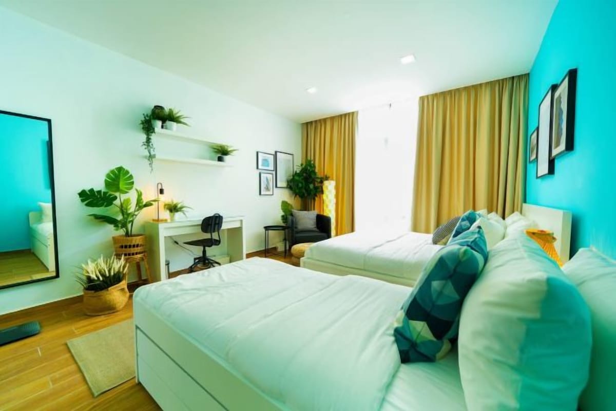 Quarto de hotel moderno com duas camas, uma escrivaninha, uma cadeira e vários vasos de plantas.