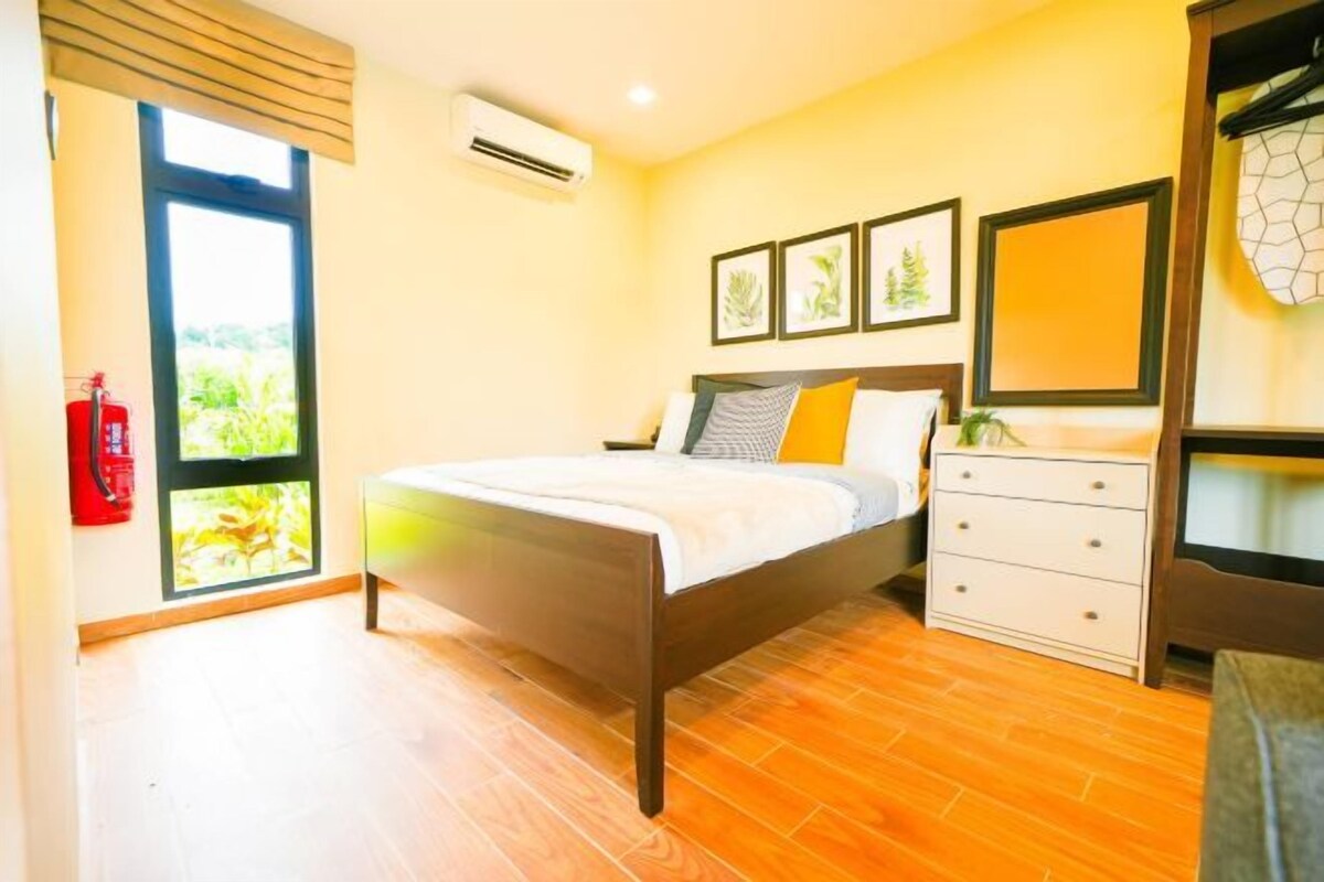 Quarto com cama de madeira, mesa de cabeceira, cômoda e quadros nas paredes.