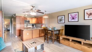 Eine moderne Wohnung mit Küche, Essbereich und Wohnzimmer. Sie verfügt über Holzschränke, einen Deckenventilator, einen Flachbildfernseher und Kunstwerke an den Wänden.