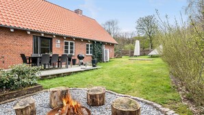 Ein Backsteinhaus mit Ziegeldach, einer Terrasse mit Gartenmöbeln und einer Feuerstelle.