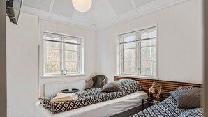 Ein kleines, helles Schlafzimmer mit zwei Betten, großen Fenstern, einem Heizkörper und einem Sessel.