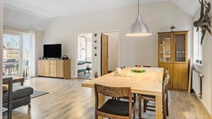 Ein geräumiger Raum mit einem Holzespeisetisch, Stühlen, einem Fernseher und einem Schrank.