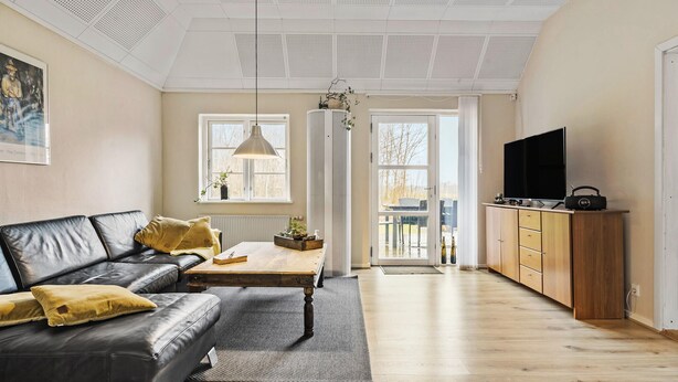 Ein modernes Wohnzimmer mit einem schwarzen Ledersofa, einem Holztisch und einem Fernseher auf einer Holzkommode.