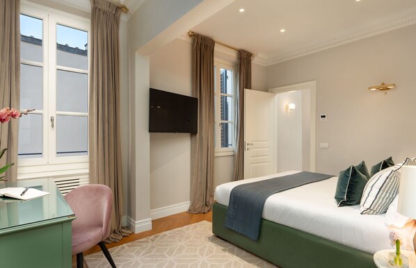 A hotel room with a bed, a desk, a chair, a TV, and a window with curtains.