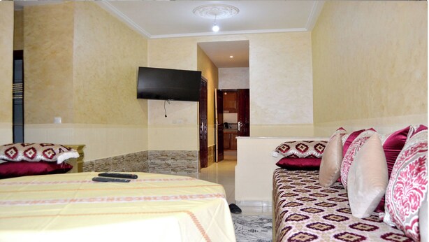 Una habitación de hotel con un conjunto de sofá, una mesita, televisor y una alfombra estampada.
