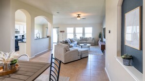 A spacious living room with a large sofa set, a coffee table, and a dining area with a wooden table and chairs. - Quaint Charm & Modern Comfort - Lovely 3 bedroom in Kyle, TX (Kyle)