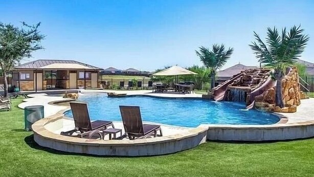 A swimming pool with a waterfall feature, surrounded by lounge chairs and palm trees. - Quaint Charm & Modern Comfort - Lovely 3 bedroom in Kyle, TX (Kyle)