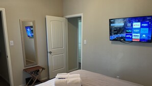 A hotel room with a bed, a TV mounted on the wall displaying streaming services, a door, and a mirror. - Quaint Charm & Modern Comfort - Lovely 3 bedroom in Kyle, TX (Kyle)