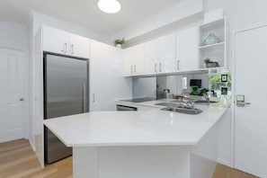A modern kitchen with white cabinetry, a stainless steel refrigerator, a central island with a sink, and a built-in oven.