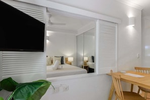A hotel room with a bed, a TV, a dining table, and a large mirror.