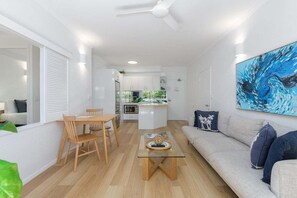 A modern living space with a dining area, a sofa, and a kitchen in the background.
