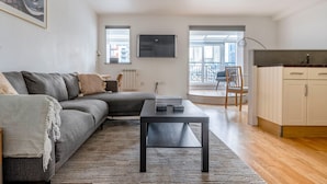 A modern living room with a grey sectional sofa, a black coffee table, and a view of the city through large windows.